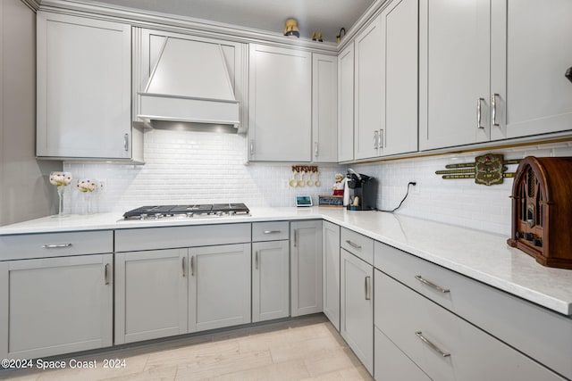 kitchen featuring stainless steel gas stovetop, premium range hood, gray cabinets, and backsplash