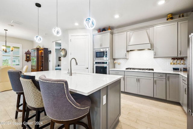 kitchen with an island with sink, appliances with stainless steel finishes, hanging light fixtures, and gray cabinets