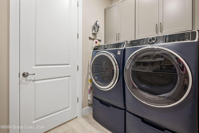 clothes washing area with light wood-style flooring, cabinet space, and washing machine and clothes dryer