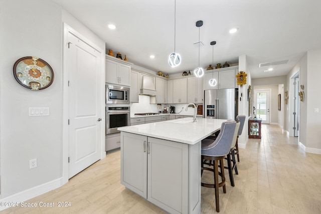 kitchen with pendant lighting, tasteful backsplash, a kitchen island with sink, stainless steel appliances, and light wood-type flooring