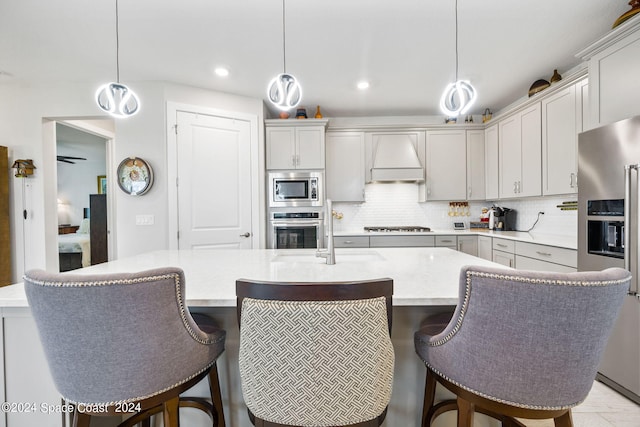 kitchen with custom range hood, hanging light fixtures, a center island with sink, and stainless steel appliances