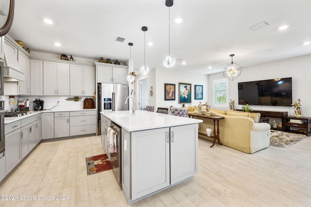 kitchen featuring light wood-type flooring, a kitchen island with sink, hanging light fixtures, and tasteful backsplash