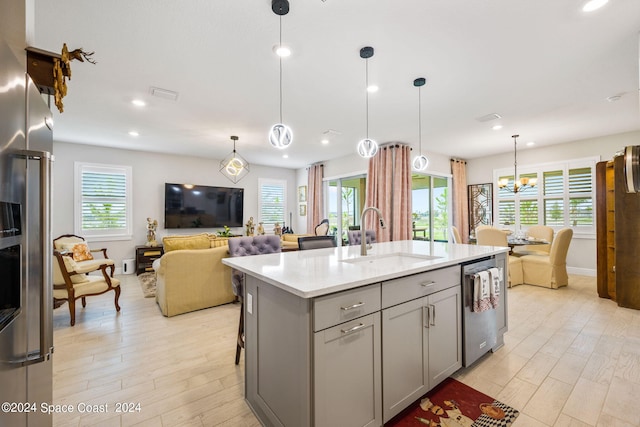 kitchen with gray cabinetry, dishwasher, decorative light fixtures, a kitchen island with sink, and sink