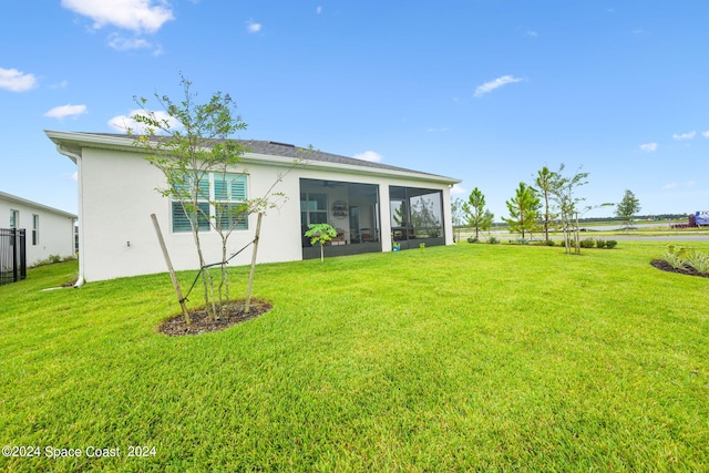 rear view of house featuring fence, a yard, stucco siding, and a sunroom