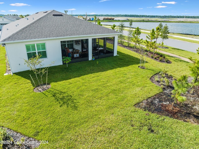 rear view of property with roof with shingles, stucco siding, a sunroom, a lawn, and a water view