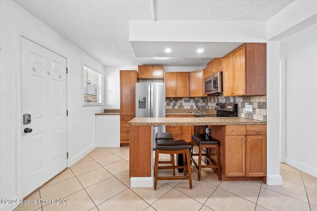 kitchen featuring light tile patterned floors, tasteful backsplash, a textured ceiling, appliances with stainless steel finishes, and a kitchen breakfast bar