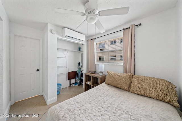 bedroom with a closet, a wall unit AC, a textured ceiling, light tile patterned flooring, and ceiling fan