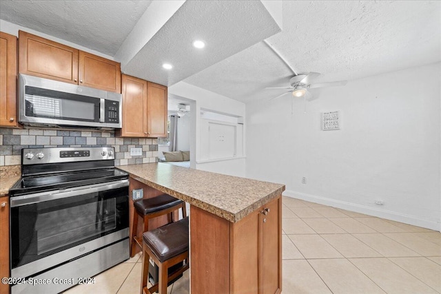 kitchen featuring a textured ceiling, ceiling fan, stainless steel appliances, and a breakfast bar