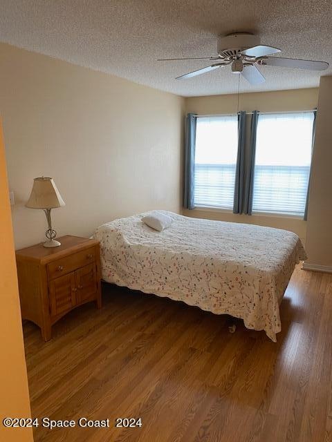 bedroom with hardwood / wood-style flooring, a textured ceiling, and ceiling fan