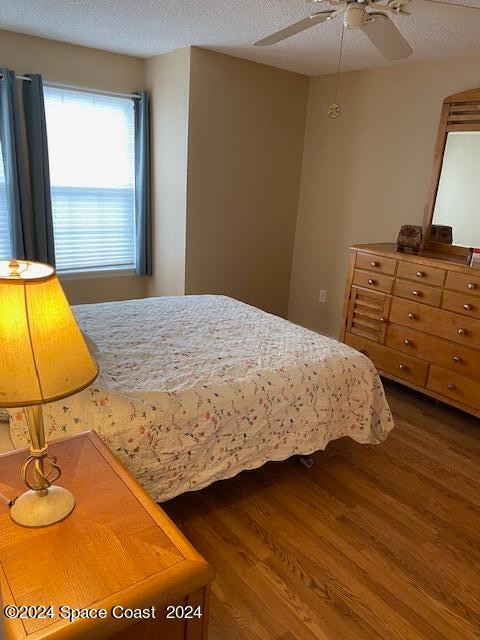 bedroom with ceiling fan, a textured ceiling, and dark hardwood / wood-style flooring