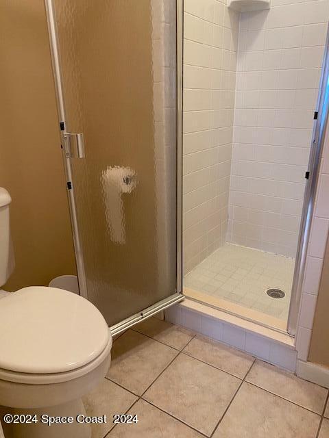 bathroom with toilet, a shower with door, and tile patterned floors