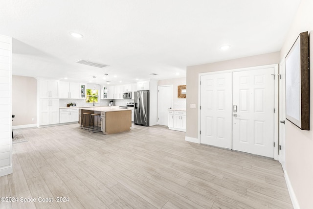 kitchen featuring a kitchen island, white cabinetry, light hardwood / wood-style flooring, appliances with stainless steel finishes, and a kitchen breakfast bar