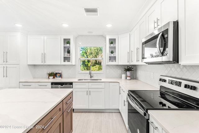 kitchen with stainless steel appliances, white cabinetry, light stone counters, and sink