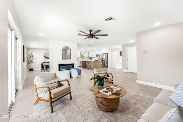 living room with ceiling fan, a large fireplace, and light hardwood / wood-style flooring