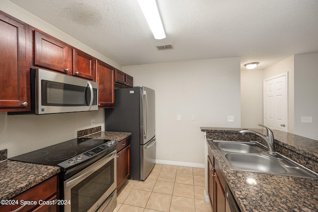 kitchen with appliances with stainless steel finishes, dark stone countertops, light tile patterned floors, a textured ceiling, and sink