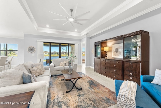 living room featuring light wood-type flooring, a tray ceiling, crown molding, and a healthy amount of sunlight