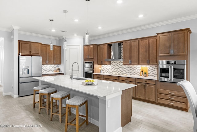 kitchen with sink, wall chimney exhaust hood, decorative light fixtures, a kitchen island with sink, and appliances with stainless steel finishes