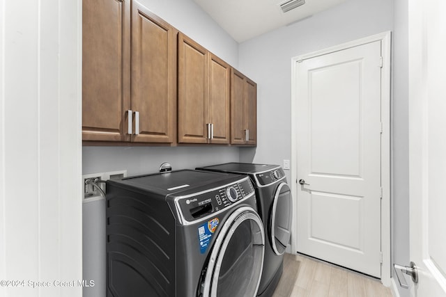 laundry room with washer and dryer, light hardwood / wood-style floors, and cabinets