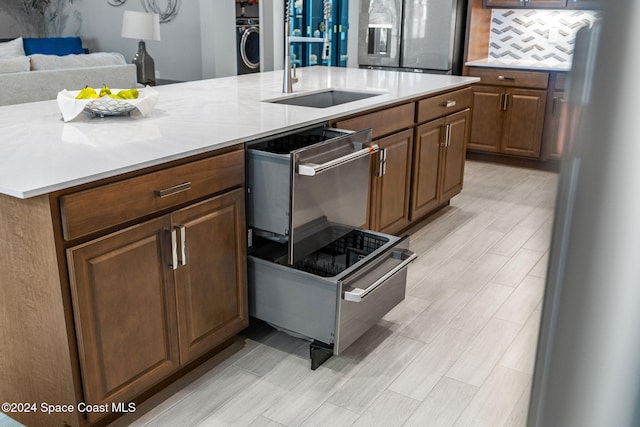 kitchen with a kitchen island with sink, sink, stainless steel refrigerator with ice dispenser, decorative backsplash, and fridge