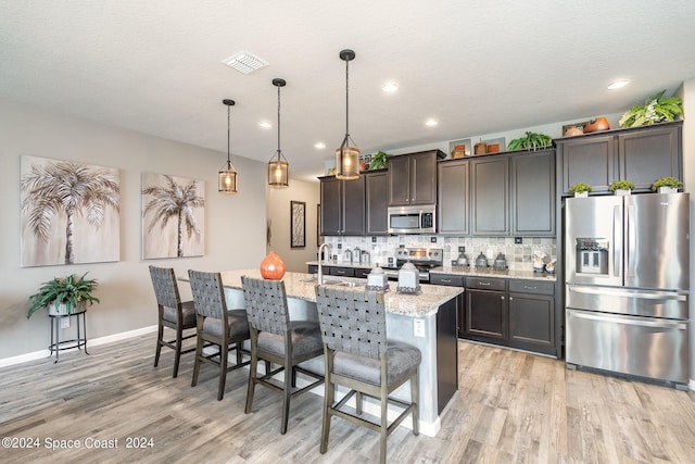 kitchen featuring a breakfast bar area, an island with sink, appliances with stainless steel finishes, decorative light fixtures, and light stone countertops