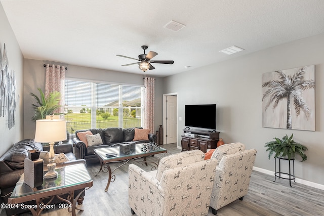 living room with light wood-type flooring, ceiling fan, and a textured ceiling