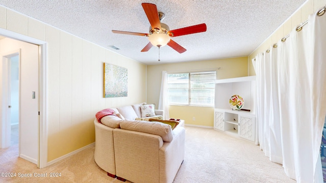 living area featuring ceiling fan, light colored carpet, and a textured ceiling