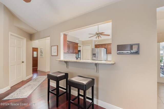 kitchen featuring hardwood / wood-style flooring, a breakfast bar area, kitchen peninsula, ceiling fan, and stainless steel fridge