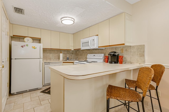 kitchen with a peninsula, visible vents, white appliances, and cream cabinetry