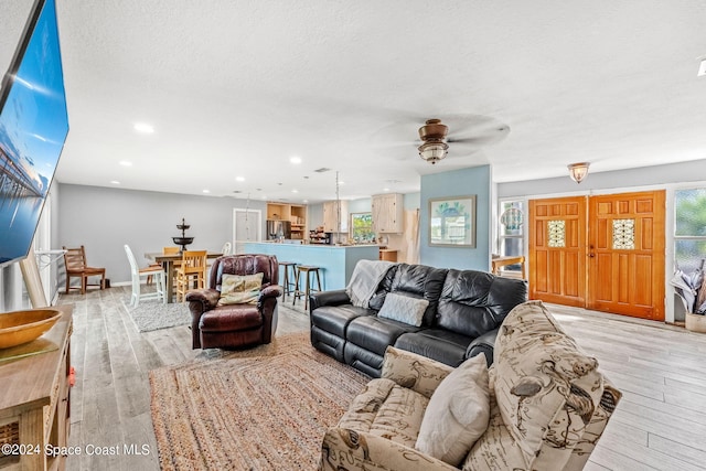 living room with a textured ceiling, light wood-type flooring, and ceiling fan