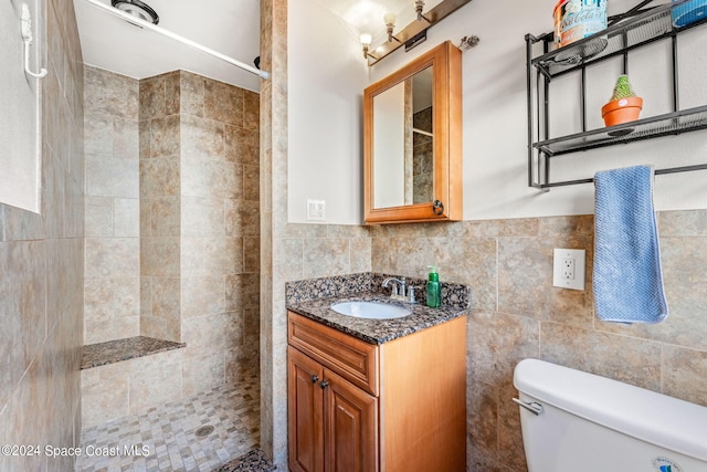 bathroom featuring toilet, vanity, a tile shower, and tile walls