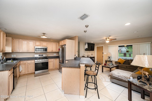 kitchen with appliances with stainless steel finishes, a kitchen breakfast bar, light brown cabinetry, ceiling fan, and decorative light fixtures