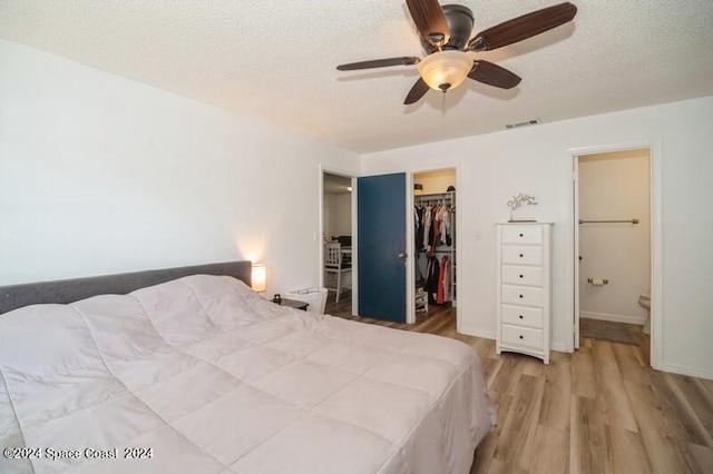 bedroom featuring a closet, hardwood / wood-style flooring, connected bathroom, a walk in closet, and ceiling fan