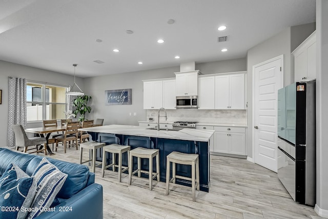 kitchen with hanging light fixtures, light hardwood / wood-style floors, white cabinets, stainless steel appliances, and sink