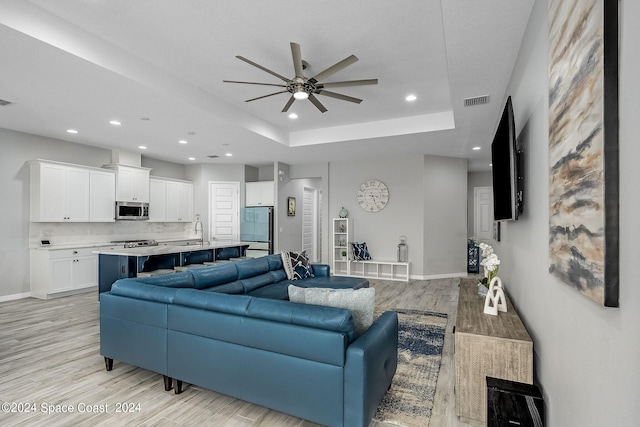 living room featuring ceiling fan, sink, a raised ceiling, and light hardwood / wood-style floors