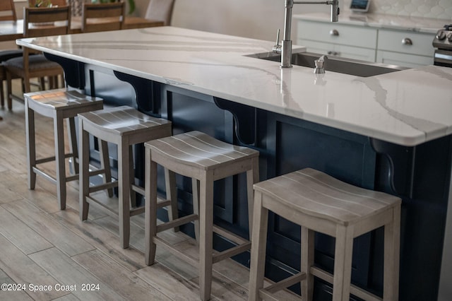 kitchen with light stone counters, a breakfast bar, backsplash, light hardwood / wood-style flooring, and sink