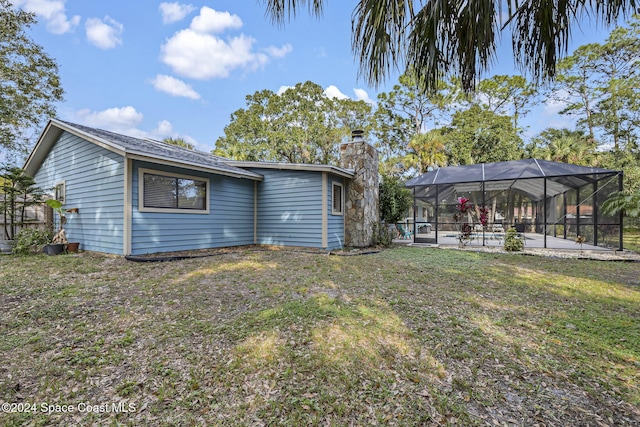 back of house with glass enclosure, a yard, and a patio