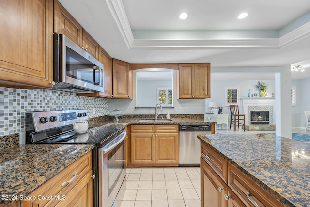 kitchen featuring sink, stainless steel appliances, dark stone counters, and a tray ceiling