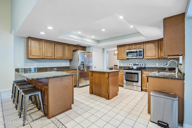 kitchen featuring sink, dark stone countertops, a tray ceiling, a kitchen island, and appliances with stainless steel finishes