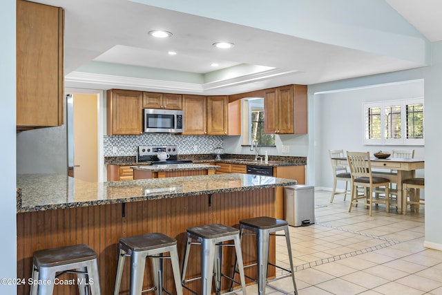 kitchen with stainless steel appliances, plenty of natural light, a breakfast bar area, and a tray ceiling