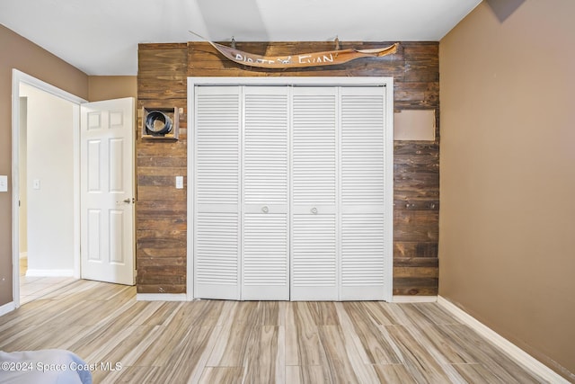 unfurnished bedroom featuring wood walls, a closet, and light wood-type flooring