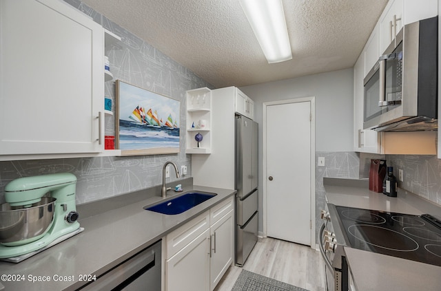 kitchen with sink, a textured ceiling, white cabinetry, appliances with stainless steel finishes, and light hardwood / wood-style floors