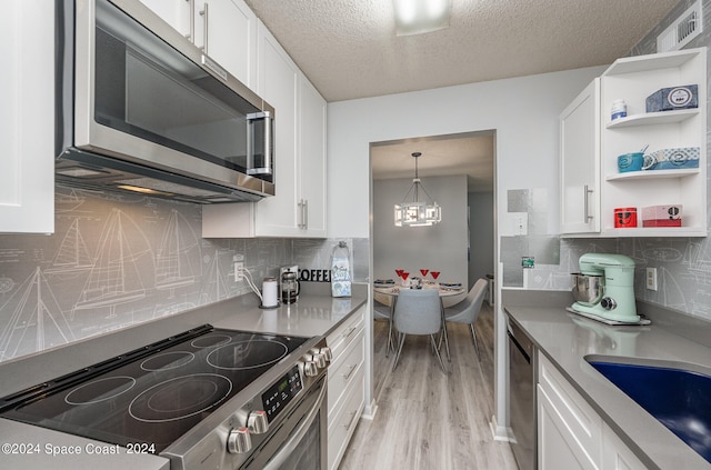 kitchen with appliances with stainless steel finishes, light hardwood / wood-style floors, white cabinetry, pendant lighting, and a textured ceiling