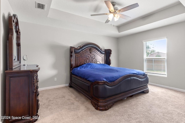 bedroom featuring a raised ceiling, ceiling fan, light colored carpet, and a textured ceiling