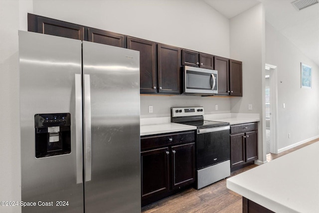 kitchen featuring dark brown cabinetry, light hardwood / wood-style floors, lofted ceiling, and stainless steel appliances