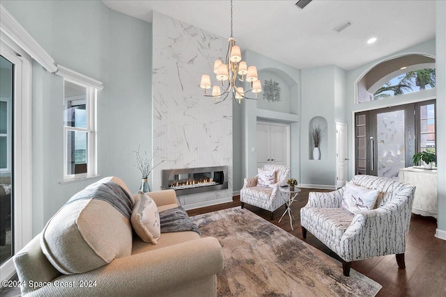 living room featuring dark wood-type flooring, a notable chandelier, a fireplace, and a towering ceiling