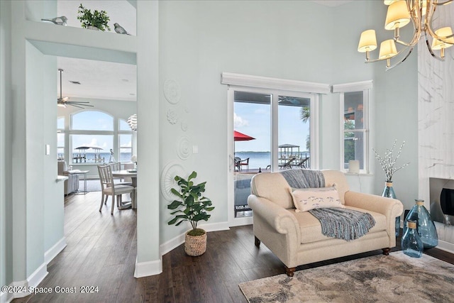 sitting room with a water view, a high ceiling, dark hardwood / wood-style floors, and ceiling fan with notable chandelier