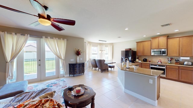 kitchen featuring a kitchen island with sink, sink, stainless steel appliances, ceiling fan, and french doors