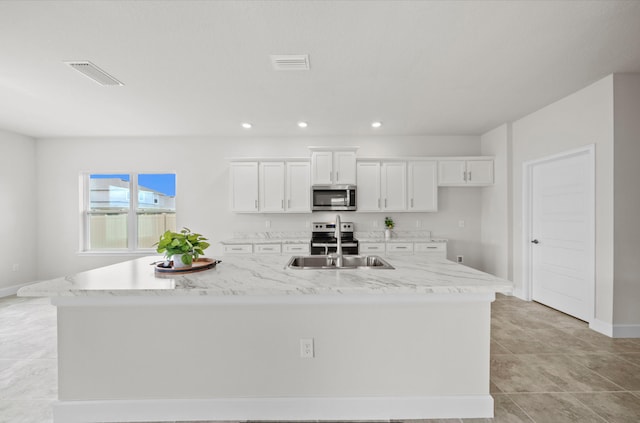 kitchen featuring light tile patterned flooring, a large island with sink, white cabinetry, stainless steel appliances, and light stone countertops