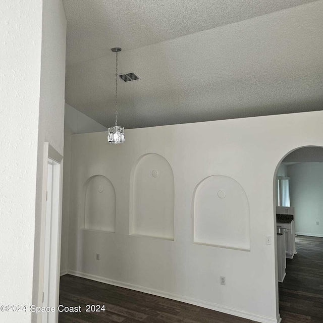 spare room with a notable chandelier, vaulted ceiling, a textured ceiling, and dark hardwood / wood-style floors