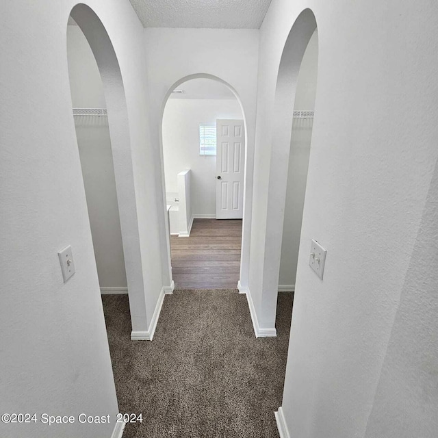 hall with a textured ceiling and dark colored carpet